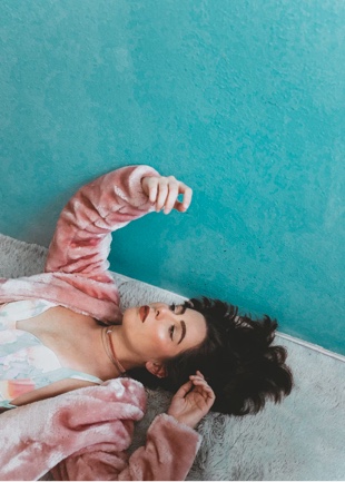 woman wearing pink fuzzy jacket laying on ground against teal background