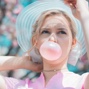 woman with blue hat blowing pink bubblegum bubble